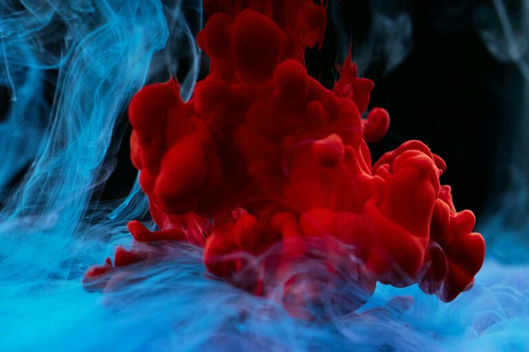 Vivid red and blue ink diffusing in water, creating a vibrant abstract pattern.